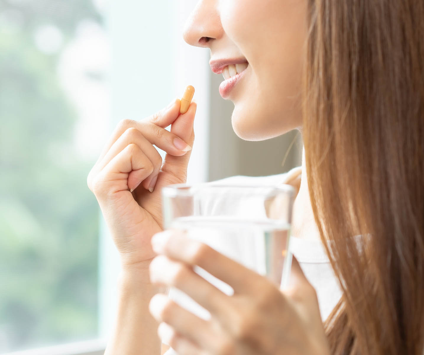 Eine Frau hält ein Glas Wasser in der Hand und nimmt Tabletten in den Mund